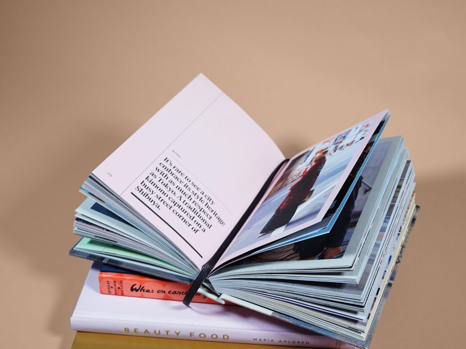 Libro abierto con texto en su página izquierda y fotografía a tamaño completo en su página derecha. El libro se encuentra encima de otros tres libros. Fondo liso beige.